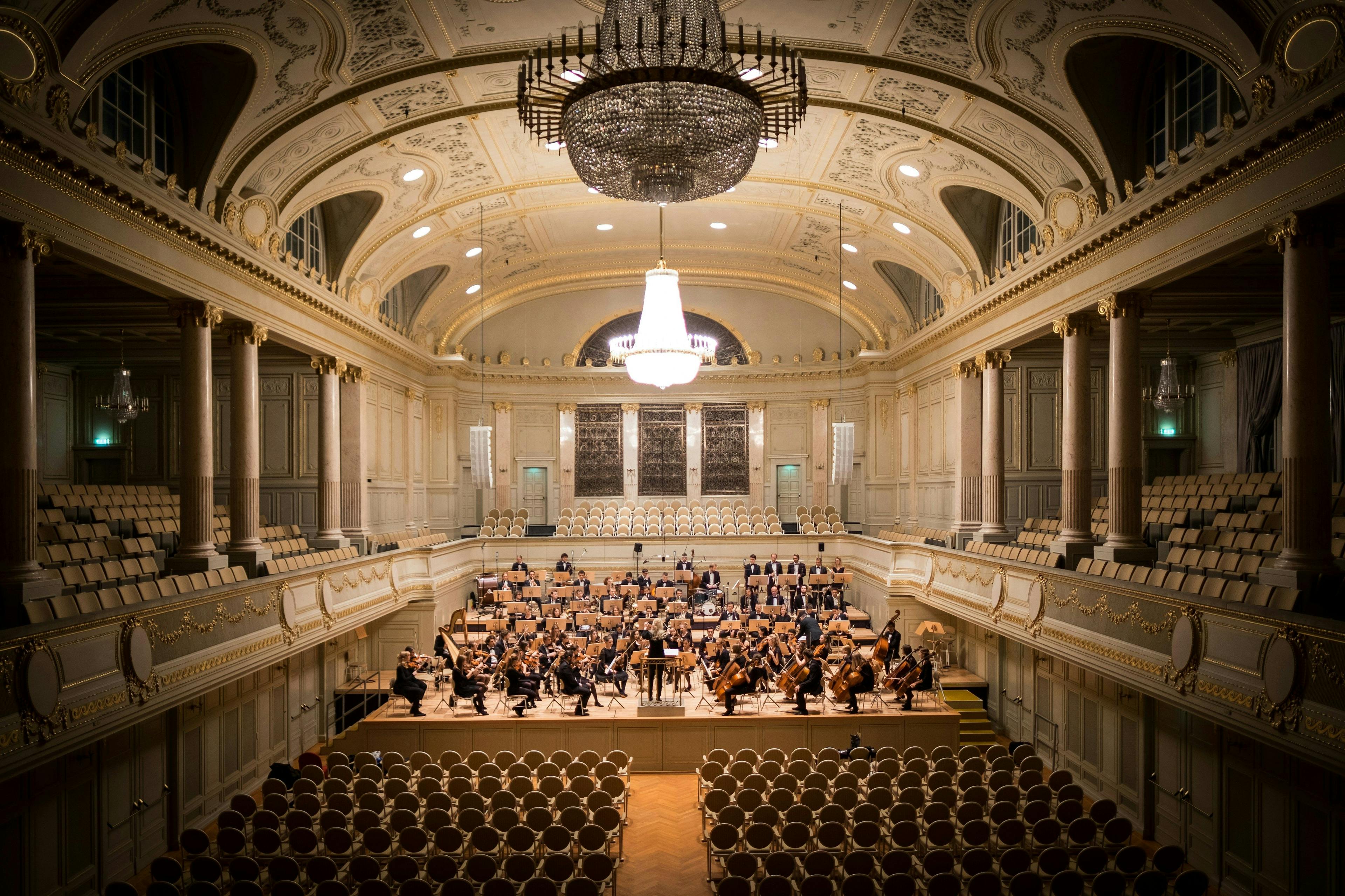 an orchestra is playing in a large auditorium with a chandelier hanging from the ceiling .