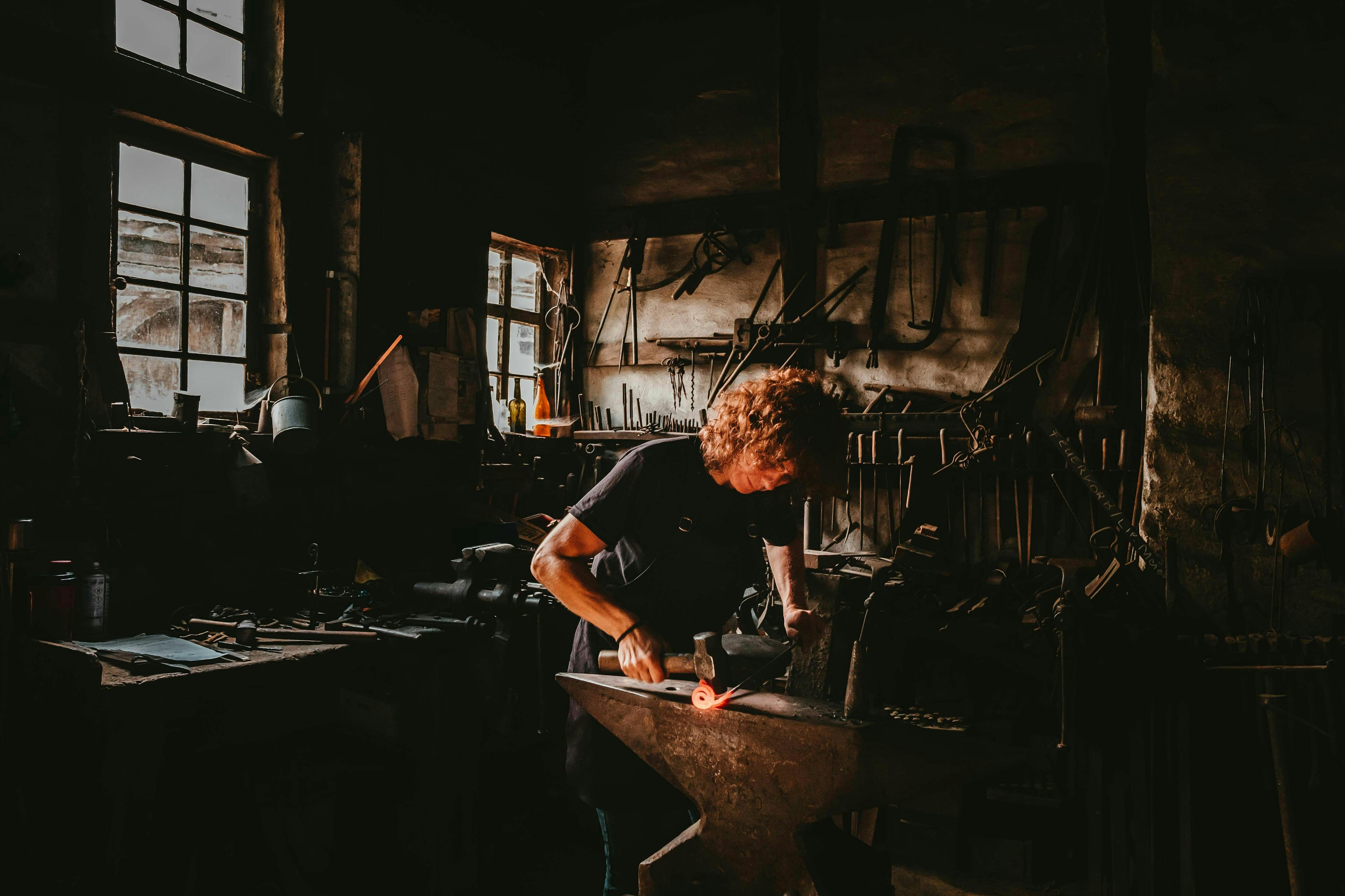en mann jobber med et stykke metall på en ambolt i et mørkt verksted.